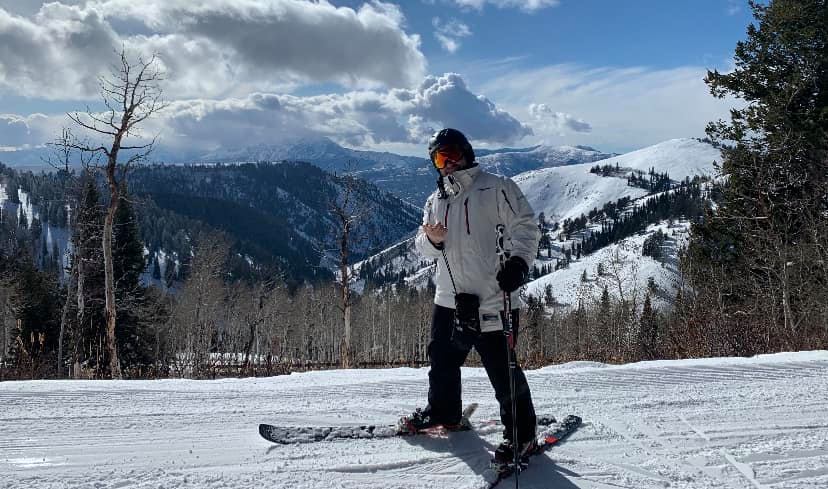 Ski the Peak Tours owner, Tom Trout, standing in skis, wearing a white winter coat, black pants, and ski goggles.