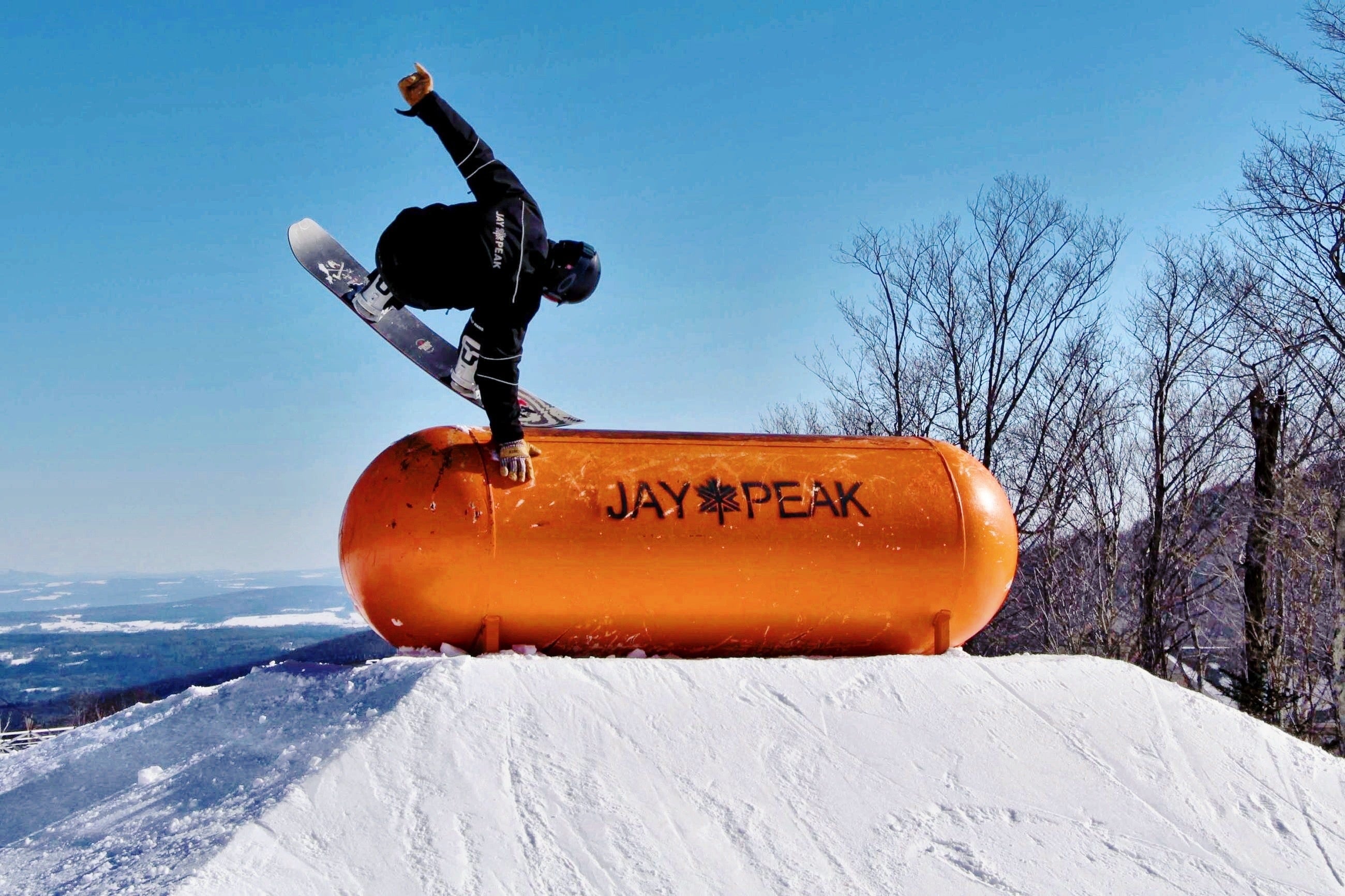 snowboarder doing a stunt on an orange tank at the top of a snowy hill