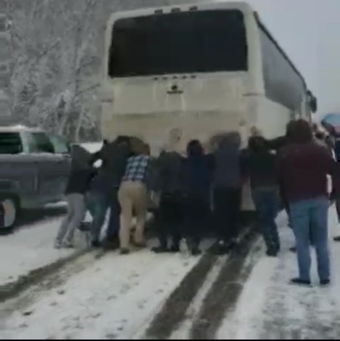 Group of people pushing large bus on a snow covered street.